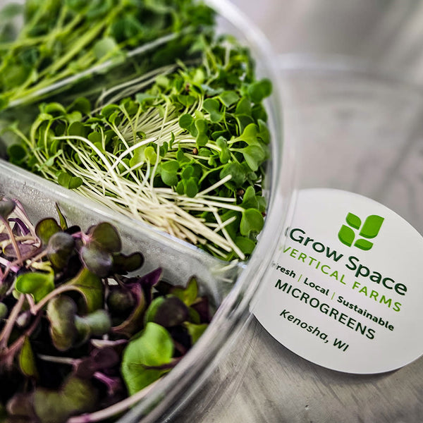A clear plastic container filled with various microgreens, including kale, cabbage, radish, and pea shoots, with the label 'Grow Space Vertical Farms' on the front.